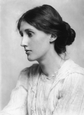 Black and white profile photograph of Virginia Woolf. She is seated facing left, with her long hair in a bun at the nape of her neck. She wears a white, long-sleeved dress. Her mouth is closed, face relaxed, and eyes appear almost unfocused.